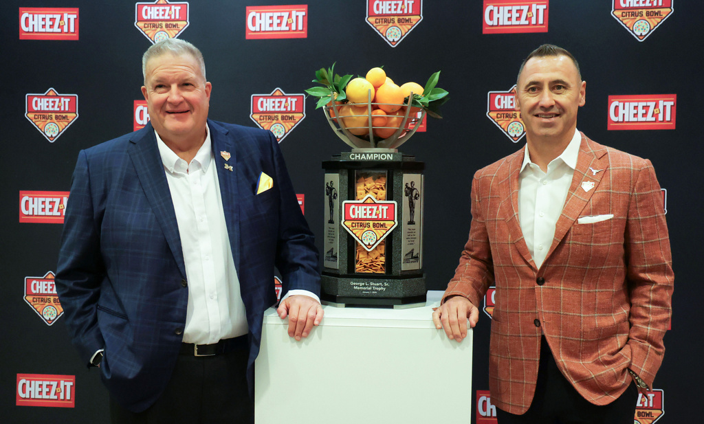 Michigan interim head coach Biff Poggi, left, and Texas head coach Steve Sarkisian, right, pose with the Citrus Bowl trophy during a NCAA college football news conference in Winter Park, Fla., Monday, Dec. 15, 2025, ahead of their teams' New Year's Eve appearance in the bowl in Orlando, Fla. (Joe Burbank/Orlando Sentinel via AP)