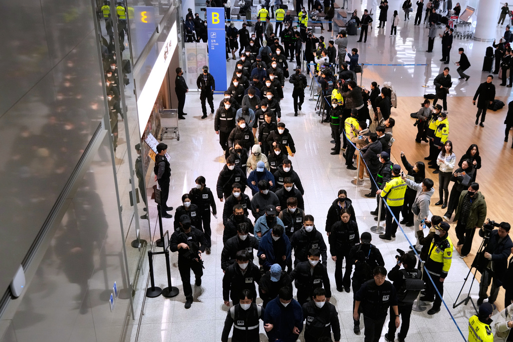 South Koreans, walking in the line at center, who are allegedly involved in online scams in Cambodia, arrive at the Incheon International Airport, in Incheon, South Korea, Friday, Jan. 23, 2026. (AP Photo/Ahn Young-joon)