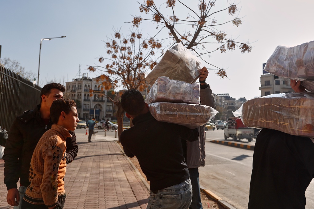 Two men carry bundles of old currency bills to deposit at the Syrian Central Bank office after authorities announced Saturday that the exchange of old Syrian pounds for new banknotes has officially begun in Damascus, Syria, Saturday, Jan. 3, 2026. (AP Photo/Omar Sanadiki)