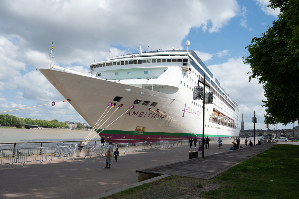 People walk past the British cruise ship Ambition, as French authorities have ordered 1,700 passengers and crew to stay on board due to a gastrointestinal illness outbreak, in Bordeaux, southwestern France, Wednesday, May 13, 2026. (AP Photo/Caroline Blumberg)