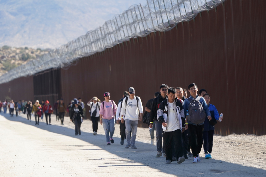 FILE - A group of people, including many from China, walk along the wall after crossing the border with Mexico to seek asylum, Oct. 24, 2023, near Jacumba, Calif. (AP Photo/Gregory Bull, File)