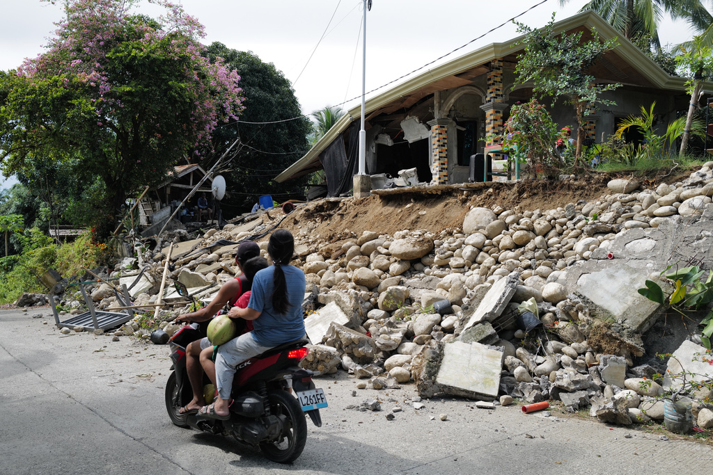 Motorists move past a house that was damaged by a strong earthquake in Manay town, Davao Oriental province, southern Philippines Saturday, Oct. 11, 2025. (AP Photo/Jeoffrey Maitem)