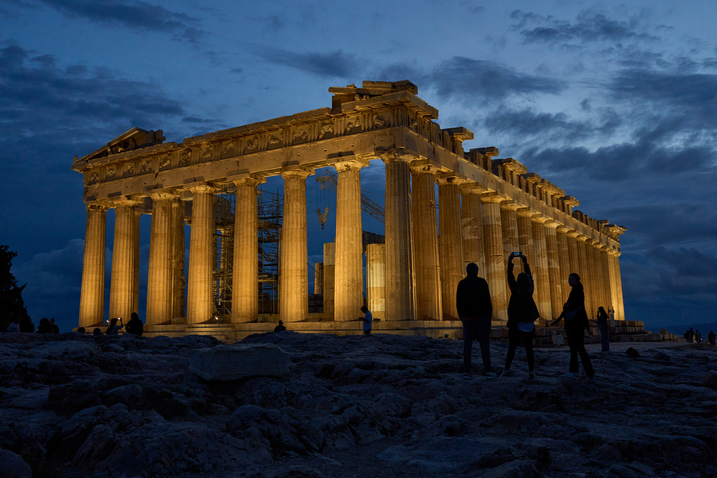 Tourists stand in front of the illuminated 5th century B.C. Parthenon temple atop the Acropolis hill in Athens, Friday, Oct. 31, 2025. (AP Photo/Petros Giannakouris)