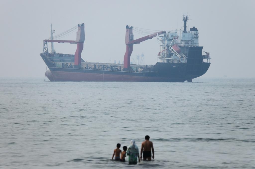 A group of people stands in shallow water as a cargo ship appears anchored in the Strait of Hormuz off Bandar Abbas, Iran, Tuesday, June 30, 2026. (Amirhosein Khorgooi/ISNA via AP)