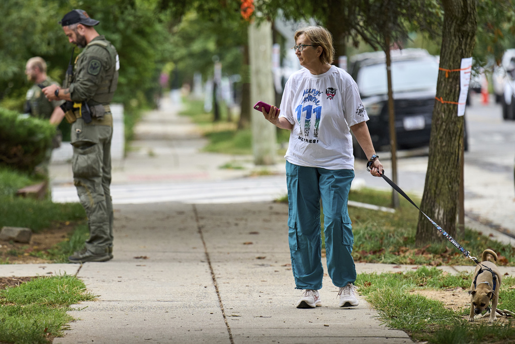 A woman walking her dog watches as officers from several federal agencies including FBI, Federal Marshalls, HSI, and Park Police, arrest a man at an apartment complex, Tuesday, Aug. 19, 2025, in the Petworth neighborhood of northwest Washington. (AP Photo/Jacquelyn Martin)