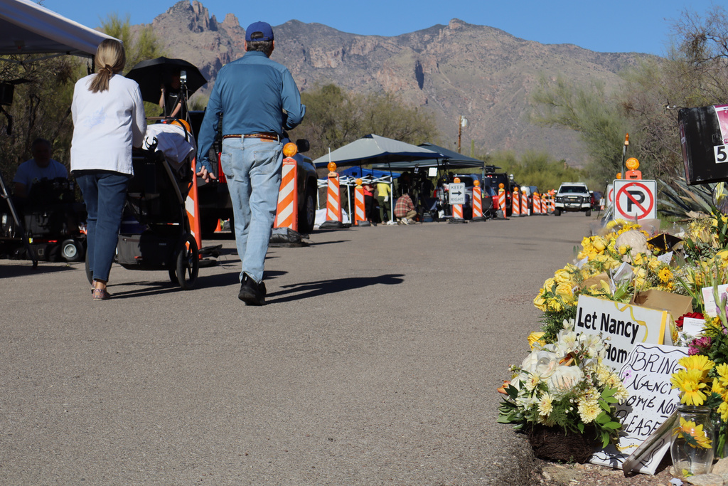 Neighbors walk by a growing memorial for Nancy Guthrie, the missing mother of "Today" show host Savannah Guthrie, outside her home in Tucson, Ariz., Sunday, Feb. 22, 2026. (AP Photo/Felicia Fonseca)