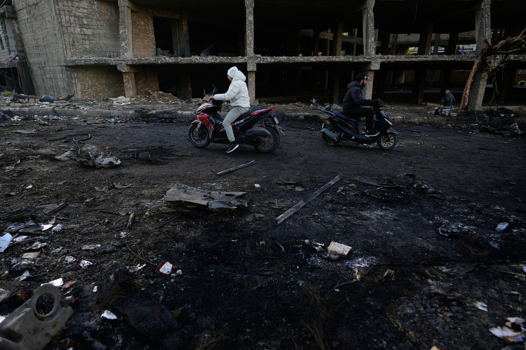 Two men ride scooters past charred debris at the site of an Israeli strike in Beirut, Lebanon, Wednesday, April 1, 2026. (AP Photo/Hassan Ammar)