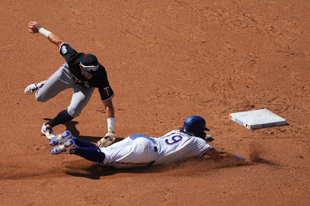 Minnesota Twins second baseman Kody Clemens, top, tags out Texas Rangers' Alejandro Osuna trying to steal the bag during the fifth inning of a baseball game Thursday, Sept. 25, 2025, in Arlington. (AP Photo/Julio Cortez)