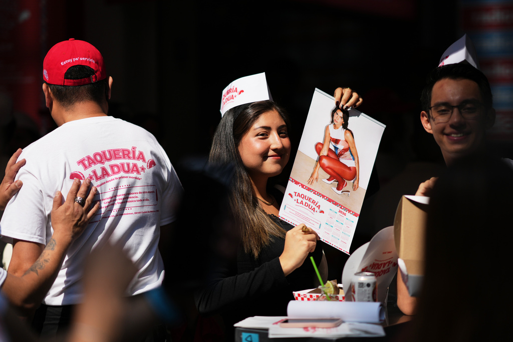 A consumer holds up a Dua Lipa calendar during the opening of the music star's taqueria, a pop-up restaurant for her fans in Mexico City, Monday, Dec. 1, 2025. (AP Photo/Eduardo Verdugo)