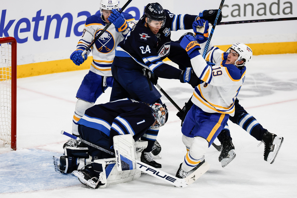 Winnipeg Jets' Logan Stanley (64) clears Buffalo Sabres' Peyton Krebs (19) from in front of goaltender Eric Comrie (1) during the second period of an NHL hockey game, in Winnipeg, Manitoba, Friday, Dec. 5, 2025. (John Woods/The Canadian Press via AP)