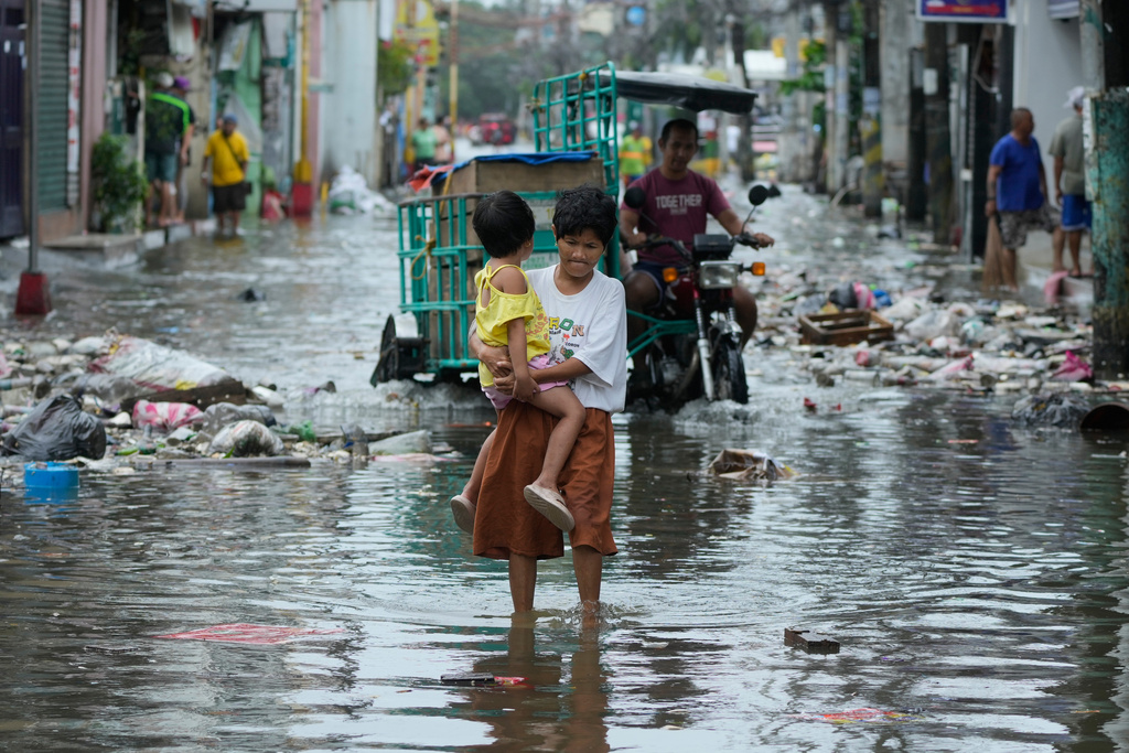 A woman and child crosses a flooded street due to Typhoon Fung-wong and high tide on Monday, Nov. 10, 2025, in Navotas, Philippines. (AP Photo/Aaron Favila)