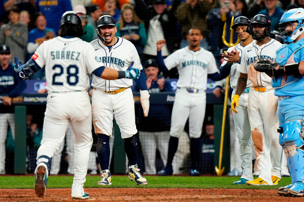 Seattle Mariners' Eugenio Suárez (28) comes in to celebrate with teammates after hitting a grand slam during the eighth inning of Game 5 of baseball's American League Championship Series against the Toronto Blue Jays in Seattle, Friday, Oct. 17, 2025. (Frank Gunn/The Canadian Press via AP)