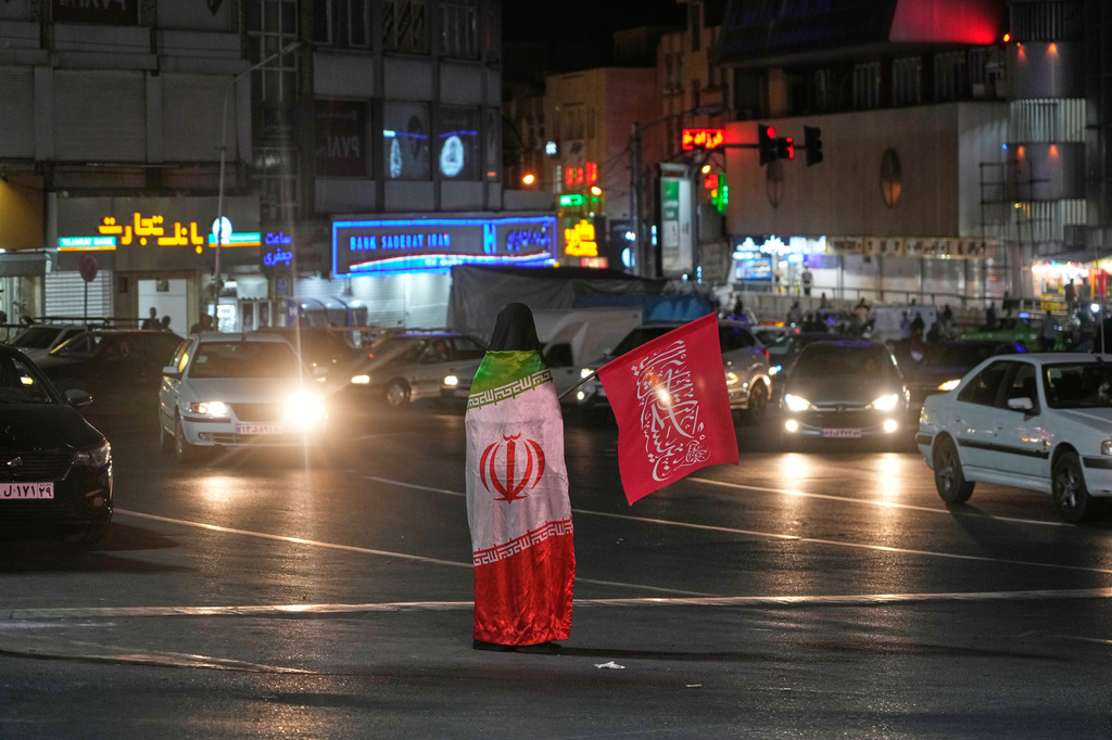 A pro-government demonstrator wears an Iranian flag as she holds a religious flag in a gathering commemorating the late Iranian Supreme Leader Ayatollah Ali Khamenei at a square in Tehran, Iran, Saturday, July 11, 2026. (AP Photo/Vahid Salemi)