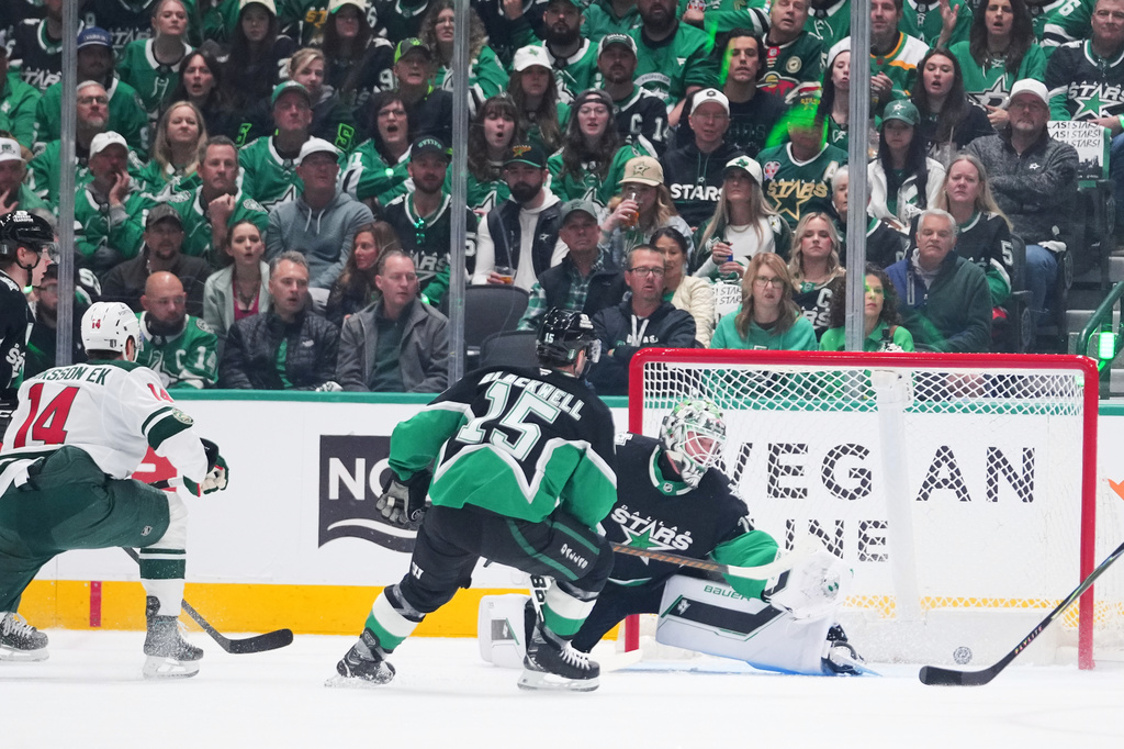 A shot by Minnesota Wild center Joel Eriksson Ek (14) enters the net of Dallas Stars goaltender Jake Oettinger, center, for a goal during the first period in Game 1 of a first-round NHL Stanley Cup playoffs hockey series, Saturday, April 18, 2026, in Dallas, Texas. (AP Photo/Julio Cortez)