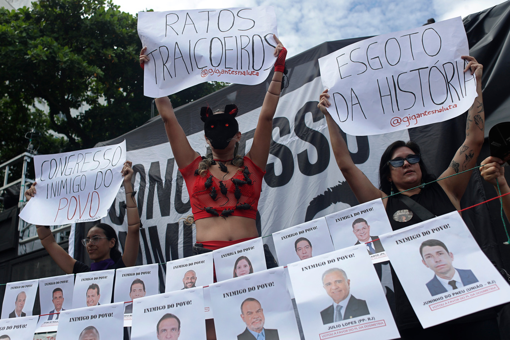 A demonstrator, center, holds up a sign with "Treacherous rats" written in Portuguese, referring to members of Congress, during a protest against a bill that looks to reduce former President Jair Bolsonaro's prison time, in Rio de Janeiro, Sunday, Dec. 14, 2025. (AP Photo/Bruna Prado)