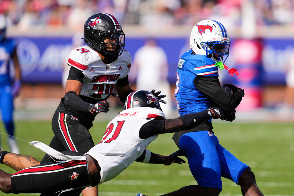 SMU wide receiver Jordan Hudson (2) catches a pass and is tackled by Louisville defensive back D'Angelo Hutchinson (21) and defensive back Corey Gordon (24) in the second half of an NCAA college football game Saturday, Nov. 22, 2025, in Dallas. (AP Photo/Tony Gutierrez)