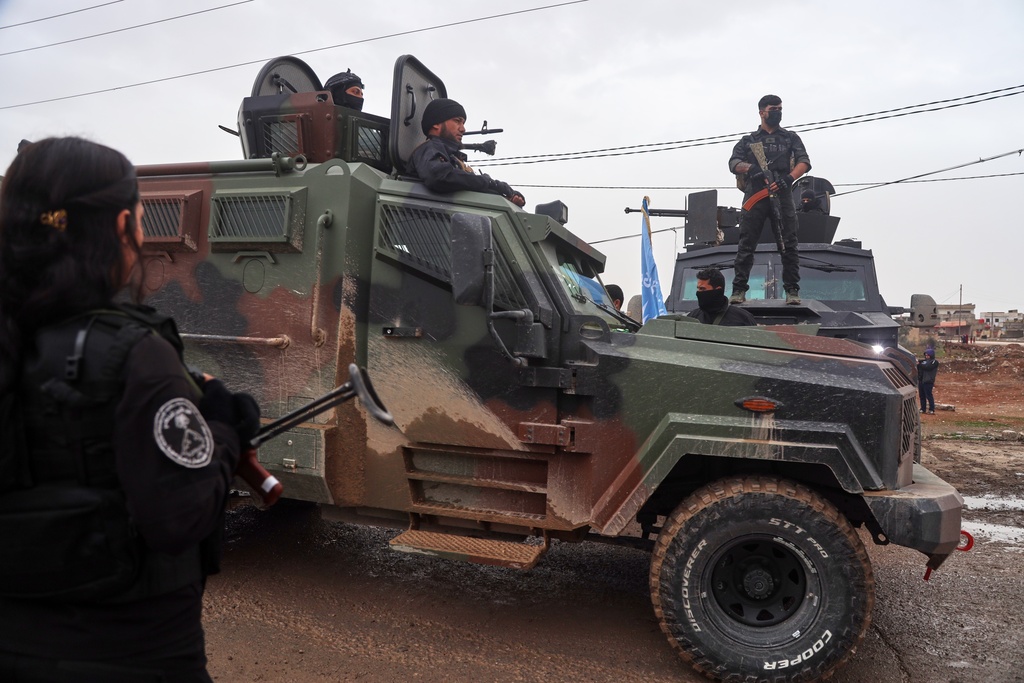 Kurdish-led Syrian Democratic Forces (SDF) soldiers, left and right, stand along the road as vehicles carrying a contingent of Syria's Interior Ministry security forces arrive to implement an agreement with the SDF aimed at stabilizing a ceasefire in al-Hassakeh, eastern Syria, Monday, Feb. 2, 2026. (AP Photo/Baderkhan Ahmad)