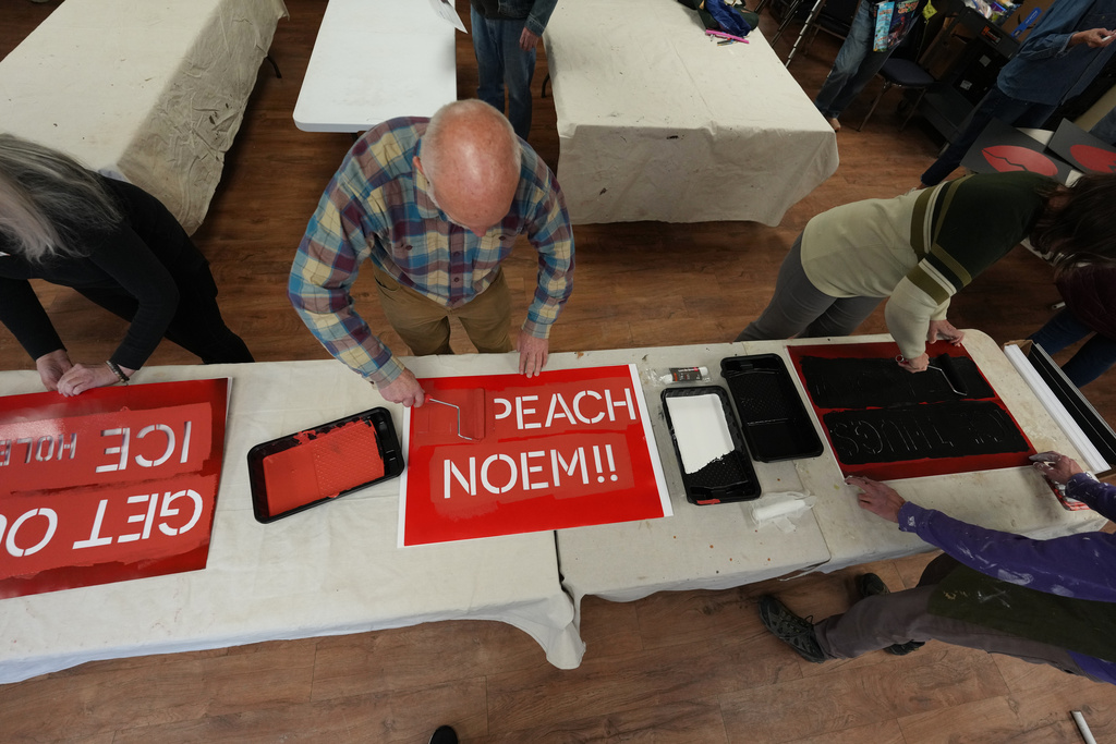 Montie Milner, center, paints a protest sign Jan. 28, 2026, in a church basement in Northglenn, Colo. (AP Photo/David Zalubowski)