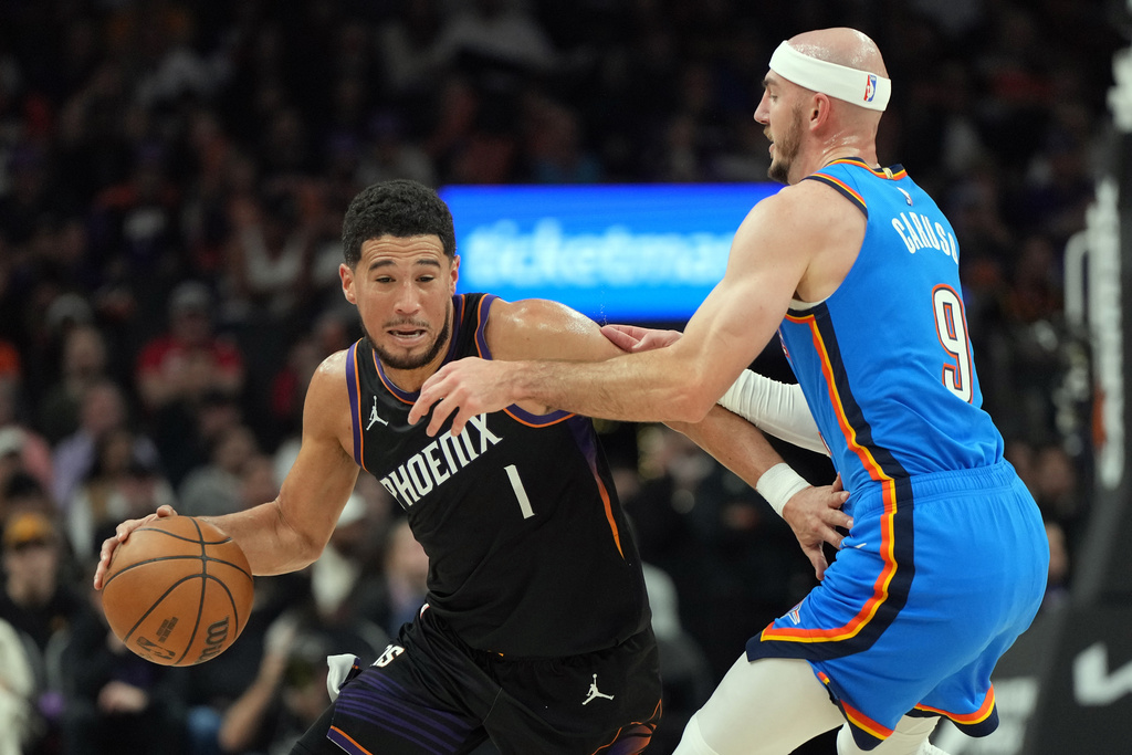 Phoenix Suns guard Devin Booker drives on Oklahoma City Thunder guard Alex Caruso (9) during the first half of an NBA basketball game, Sunday, Jan. 4, 2026, in Phoenix. (AP Photo/Rick Scuteri)