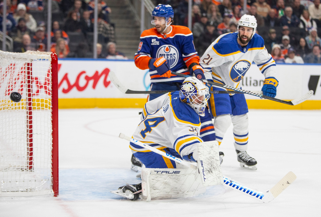 Buffalo Sabres goalie Alex Lyon (34) bats the puck away as Edmonton Oilers Adam Henrique (19) and Conor Timmins (21) look on during second period NHL action in Edmonton, Tuesday, Dec. 9, 2025. (Amber Bracken/The Canadian Press via AP)