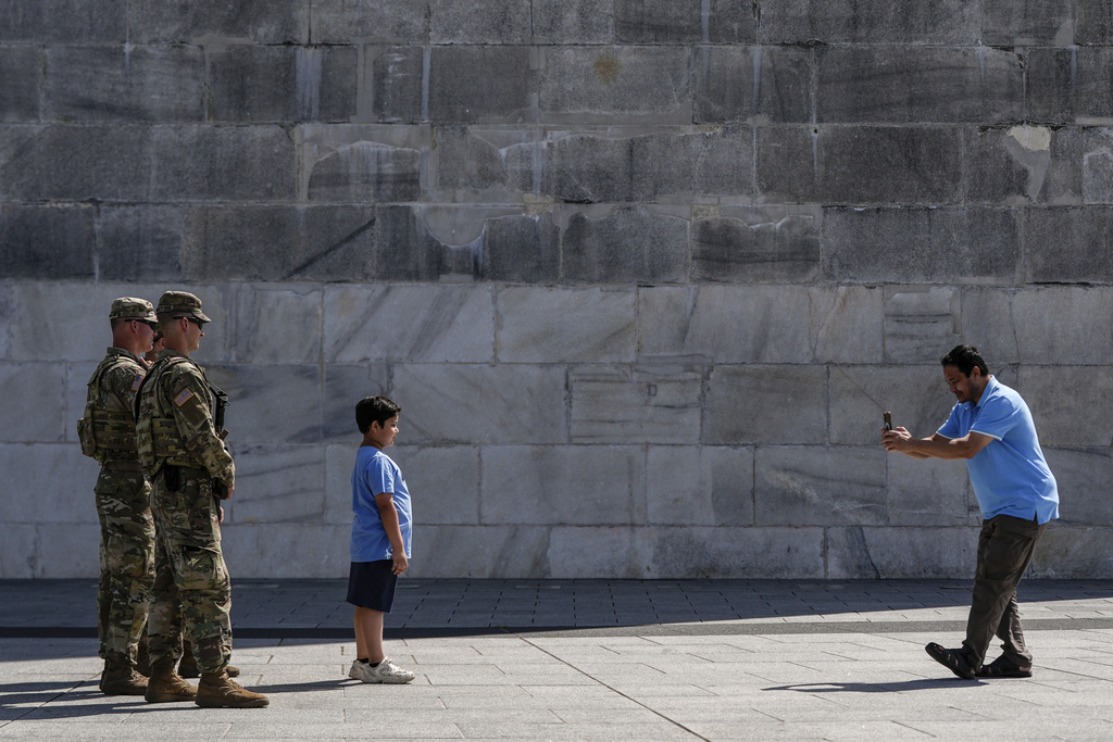 Armed National Guardsmen pose for a photo with a boy while patrolling at the base of the Washington Monument, Tuesday, Aug. 26, 2025, in Washington. (AP Photo/Julia Demaree Nikhinson)