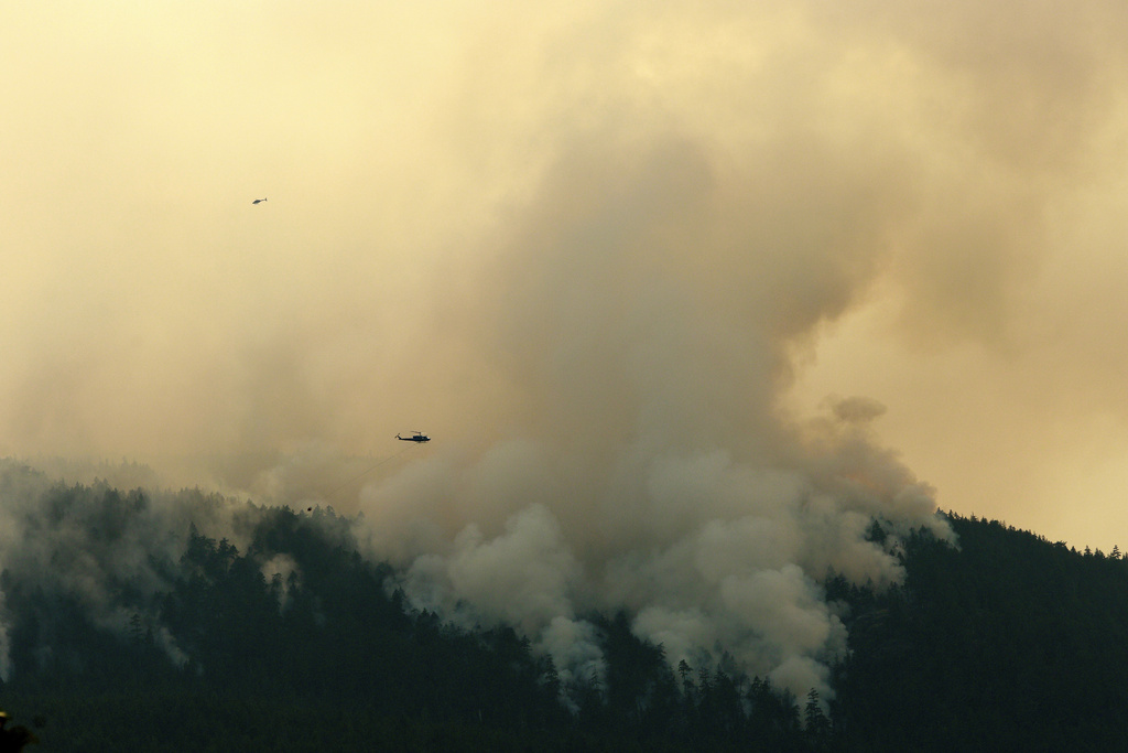FILE - A helicopter flies by the Wesley Ridge wildfire near Cameron Lake where an out-of-control fire continues to burn near Coombs, British Columbia, Aug. 3, 2025. (Chad Hipolito/The Canadian Press via AP)