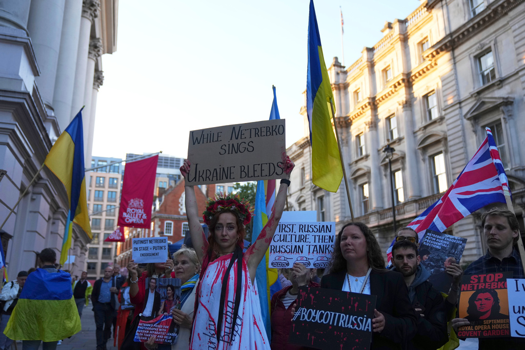 Pro-Ukraine protesters hold up placards and flags during a demonstration against the Royal Opera House in London, as the house had set an Russian opera singer to perform the lead in Puccini's Tosca, Thursday, Sept. 11, 2025. (AP Photo/Joanna Chan)