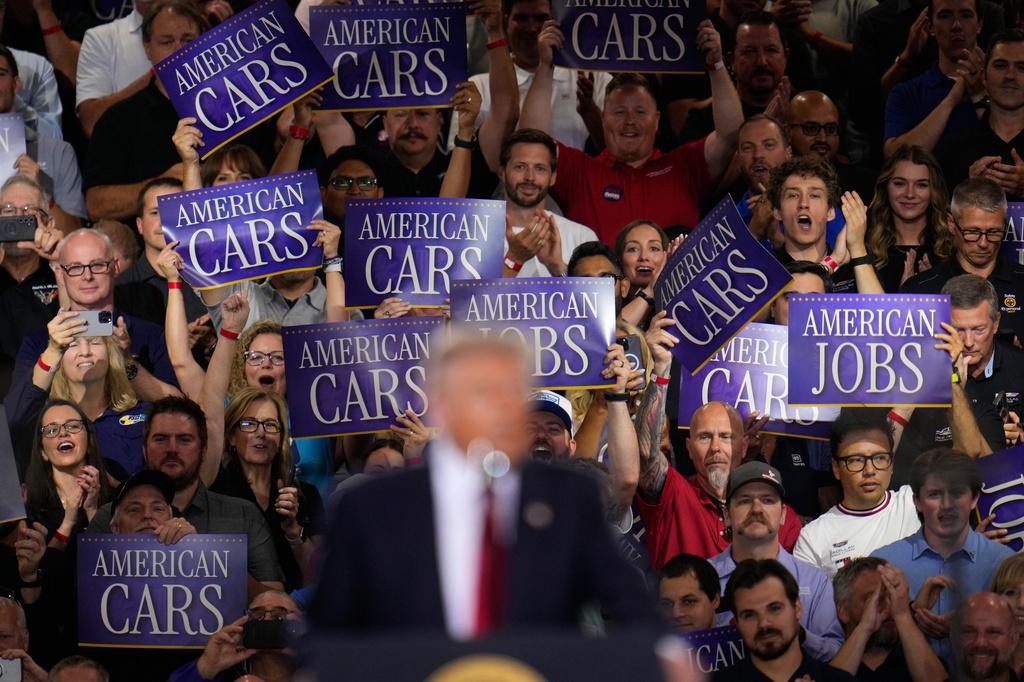 Attendees hold signs as President Donald Trump speaks at the General Motors Proving Ground, Monday, July 27, 2026, in Milford, Mich. (AP Photo/Paul Sancya)