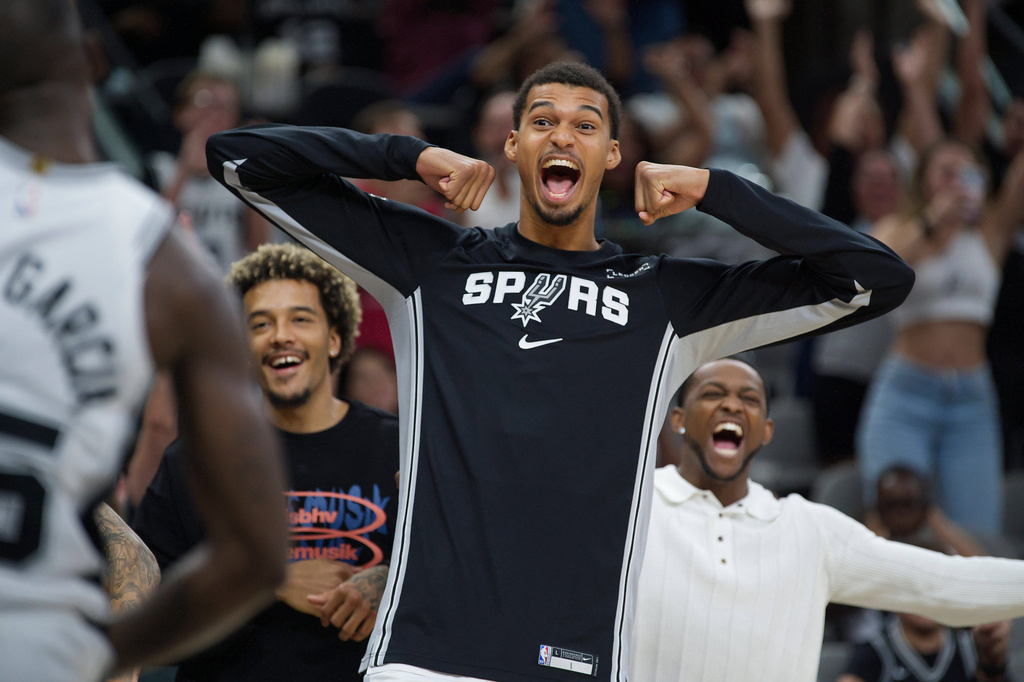 San Antonio Spurs center Victor Wembanyama, center, celebrates after a basket by Spurs guard David Jones Garcia, left, in overtime during a preseason NBA basketball game against the Utah Jazz, Friday, Oct. 10, 2025, in San Antonio. (AP Photo/Darren Abate)