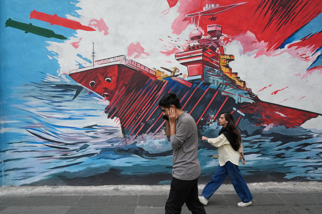 People walk past a mural depicting a U.S. aircraft carrier under missile attack in downtown Tehran, Iran, Sunday, May 17, 2026. (AP Photo/Vahid Salemi)