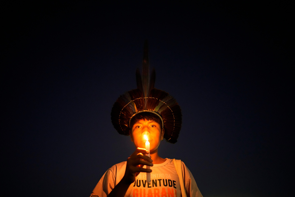An Indigenous youth holds a candle during a protest calling for the protection of Indigenous land rights and demarcations outside the Supreme Court in Brasilia, Brazil, Tuesday, Aug. 11, 2026. (AP Photo/Eraldo Peres)