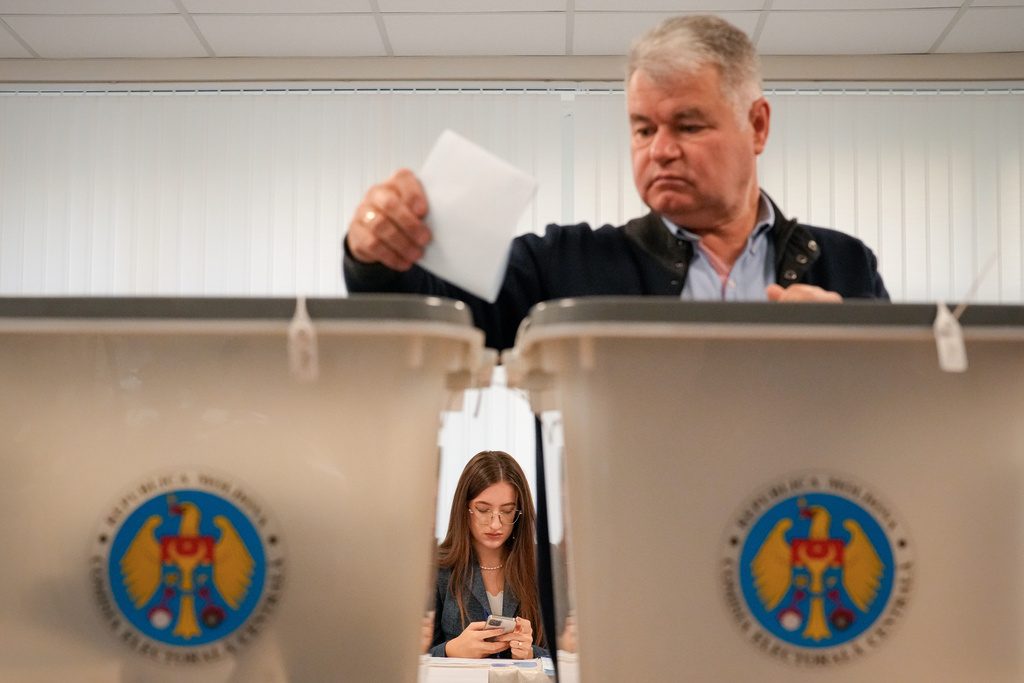 A man casts his vote as an election official attents to a voting station during a parliamentary election, in Chisinau, Moldova, Sunday, Sept. 28, 2025. (AP Photo/Vadim Ghirda)