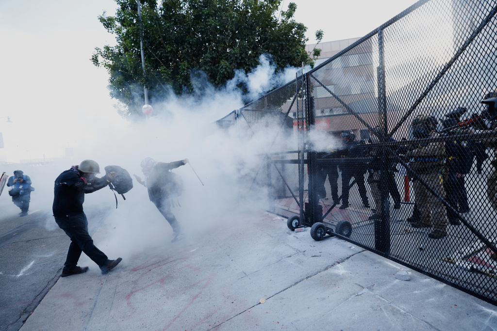 Demonstrators take cover as police fire tear gas outside the Metropolitan Detention Center in downtown Los Angeles during a "No Kings" protest Saturday, March 28, 2026. (AP Photo/Jill Connelly)