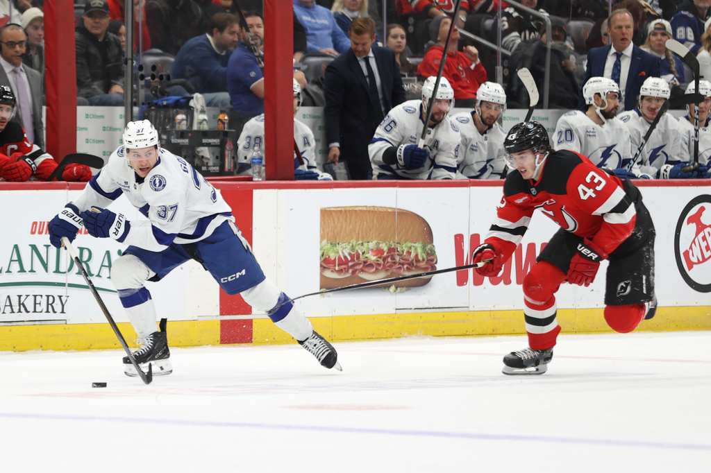 New Jersey Devils' Luke Hughes (43) attempts to steal the puck from Tampa Bay Lightning's Yanni Gourde (37) during the first period of an NHL hockey game Thursday, Dec. 11, 2025, in Newark, N.J. (AP Photo/Pamela Smith)