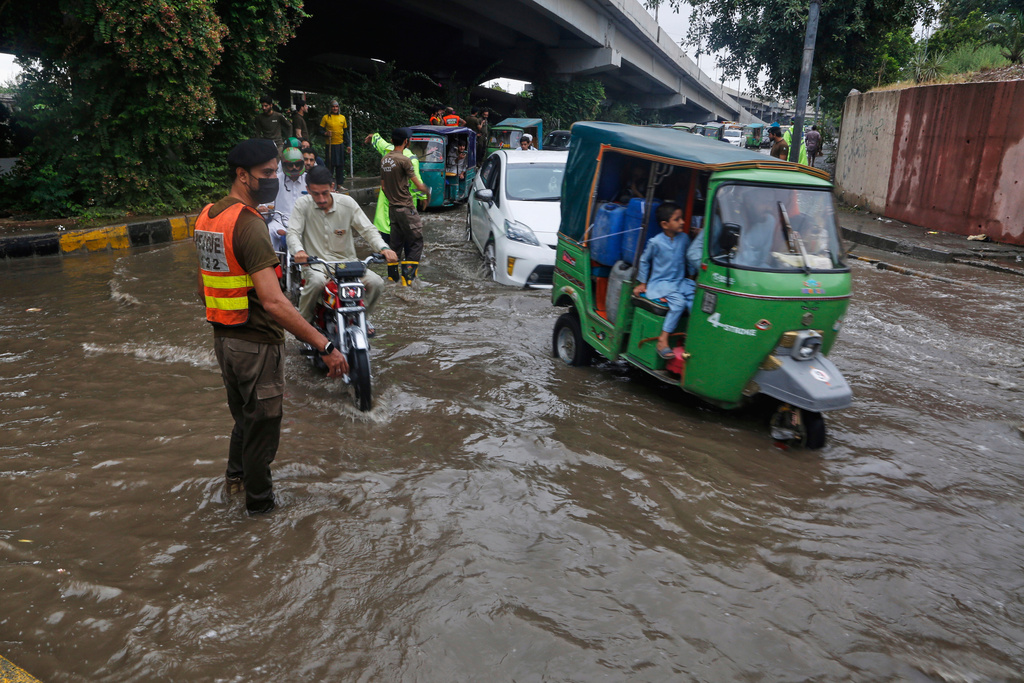 A police officer directs vehicles and motorcyclists driving through a flooded road after heavy rainfall in Peshawar, Pakistan, Monday, Aug. 18, 2025. (AP Photo/Muhammad Sajjad)