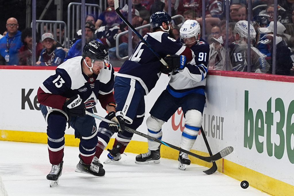 Colorado Avalanche right wing Valeri Nichushkin, left, collects the puck as defenseman Brent Burns, back left, checks Winnipeg Jets center Cole Perfetti (91) in the second period of an NHL hockey game Saturday, March 28, 2026, in Denver. (AP Photo/David Zalubowski)