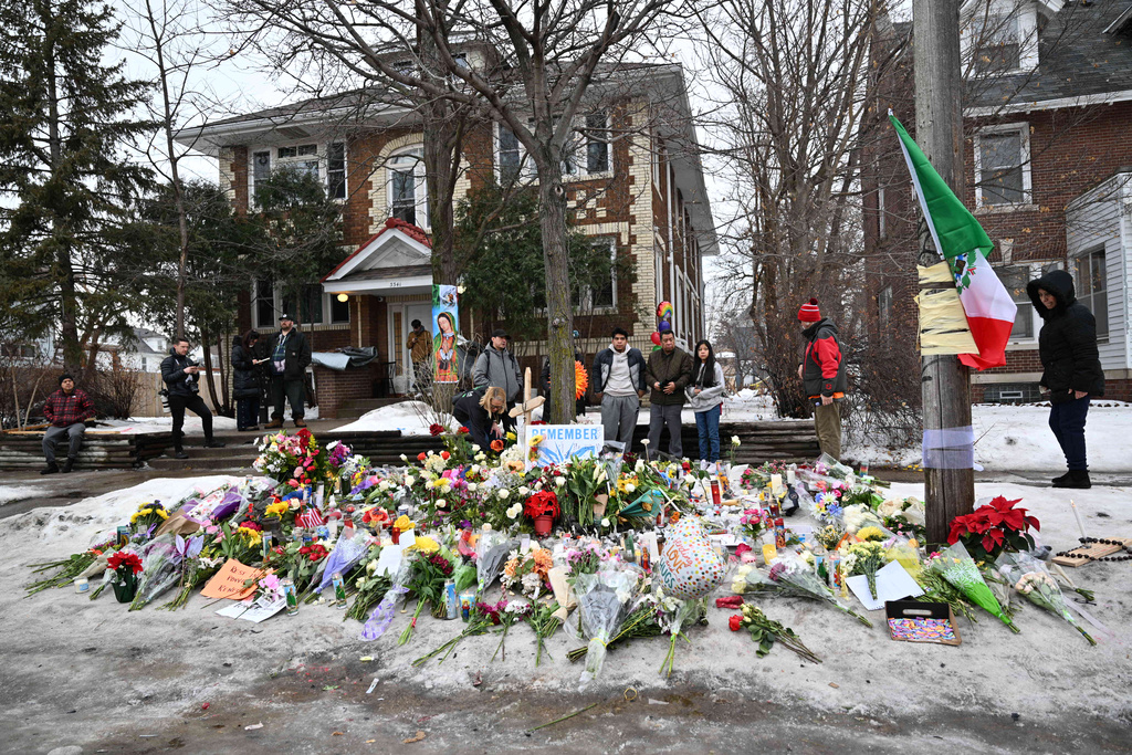 People gather around a makeshift memorial honoring Renee Good who was fatally shot by a federal law enforcement agent near the site of the shooting in Minneapolis, Thursday, Jan. 8, 2026. (AP Photo/Tom Baker)