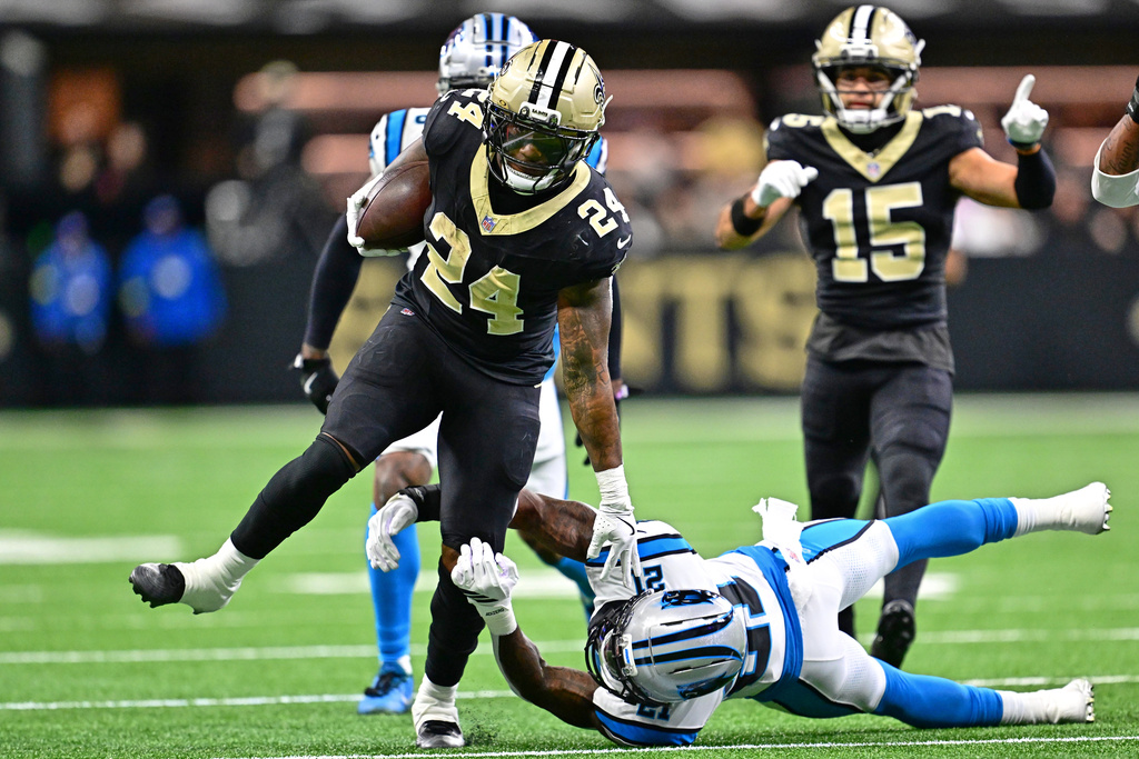 CORRECTS TO DEVIN NEAL, NOT BURGESS - New Orleans Saints running back Devin Neal (24) runs the ball against Carolina Panthers safety Nick Scott (21) in the first half of an NFL football game Sunday, Dec. 14, 2025, in New Orleans. (AP Photo/Ella Hall)
