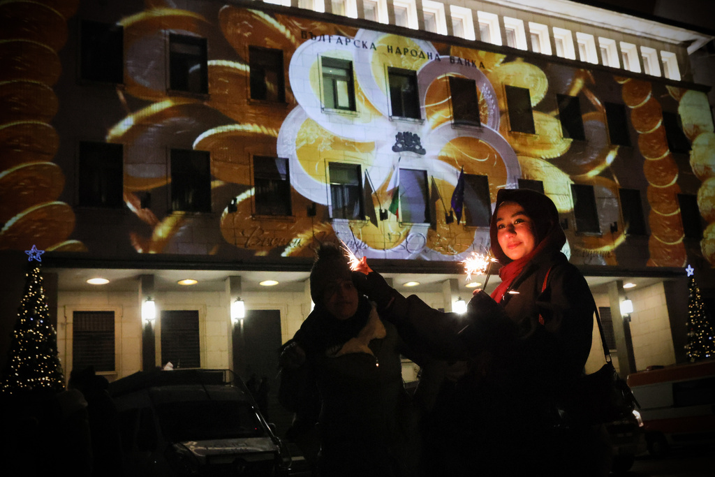 A woman holds sparklers during the celebration of the New Year and Bulgaria's adoption of euro in front of Bulgarian National Bank in Sofia, enlighten by Euro coins projection, Thursday Jan. 1, 2026. (AP Photo/Valentina Petrova)