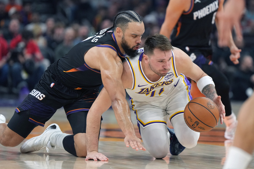 Phoenix Suns forward Dillon Brooks, left, and Los Angeles Lakers guard Luka Doncic, right, battle for the ball during the first half of an NBA basketball game, Sunday, Dec. 14, 2025, in Phoenix. (AP Photo/Rick Scuteri)