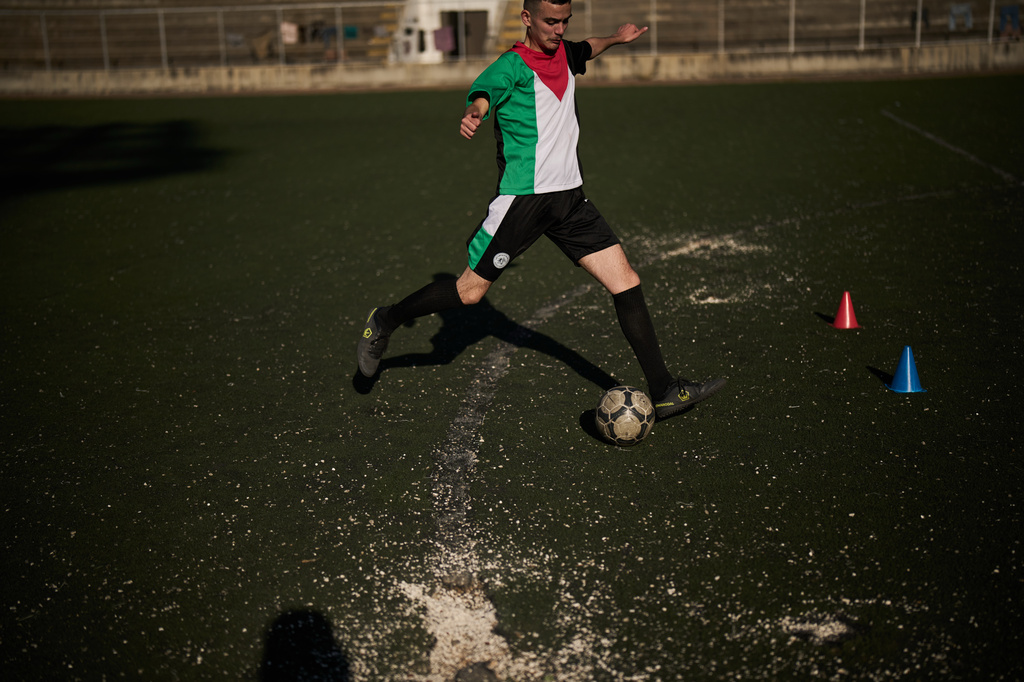 A youth from a local soccer academy, wearing a jersey in the colors of the Palestinian flag, kicks a ball during a practice session on a worn municipal stadium pitch in the West Bank city of Nablus, Thursday, May 7, 2026. (AP Photo/Leo Correa)