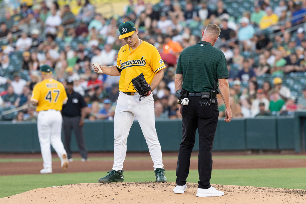 Athletics' trainer checks on pitcher J.T. Ginn, left, after catching a line drive hit by Texas Rangers' Brandon Nimmo during the 2-3 inning of a baseball game Saturday, Aug. 15, 2026, in West Sacramento, Calif. (AP Photo/Sara Nevis)
