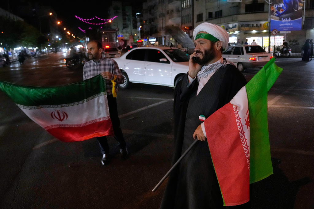 A cleric speaks on his cellphone holding an Iranian flags for a pro-government campaign in downtown Tehran, Iran, Friday, May 8, 2026. (AP Photo/Vahid Salemi)