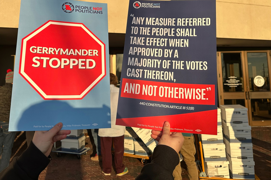 An opponent of new Missouri congressional districts approved by the Republican-led legislature holds signs outside the secretary of state's office in Jefferson City, Missouri, on Tuesday, Dec. 9, 2025, as petitions calling for a referendum election are delivered. (AP Photo/David A. Lieb)