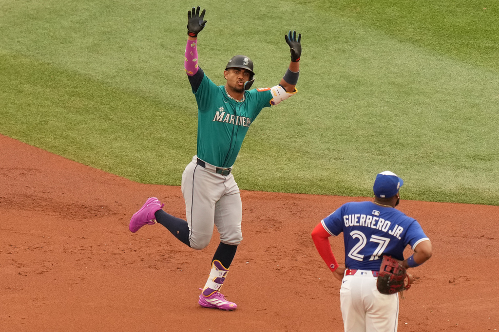 Seattle Mariners' Julio Rodríguez, left, rounds the bases after hitting a three-run home run as Toronto Blue Jays first baseman Vladimir Guerrero Jr. (27) looks on during the first inning of Game 2 of baseball's American League Division Series in Toronto, Monday, Oct. 13, 2025. (Chris Young/The Canadian Press via AP)
