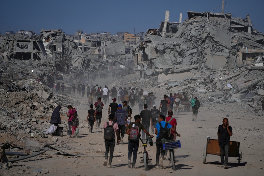 Displaced Palestinians walk past destroyed buildings as they return to their homes in the Zeitoun neighborhood of Gaza City, Friday, Oct. 10, 2025, after Israel and Hamas agreed on a ceasefire and the release of remaining hostages. (AP Photo/Jehad Alshrafi)