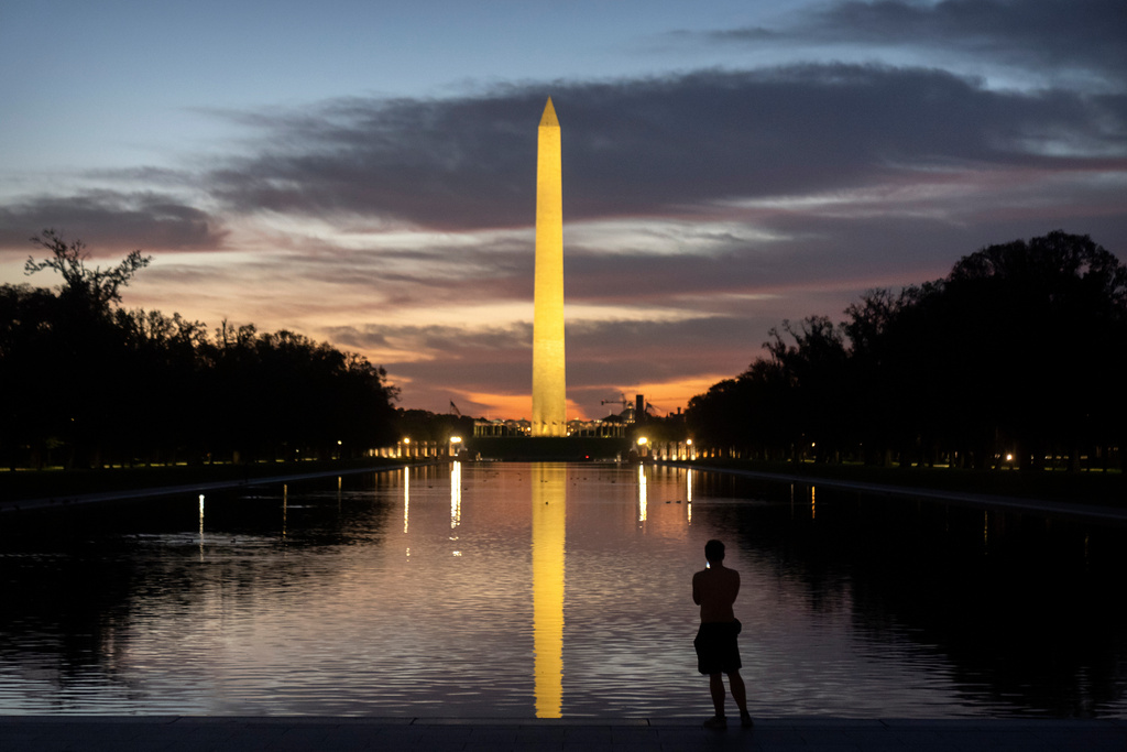 A visitor stands along the reflecting pool near the Washington Monument at dawn on Wednesday, Oct. 1, 2025, in Washington. (AP Photo/Mark Schiefelbein)