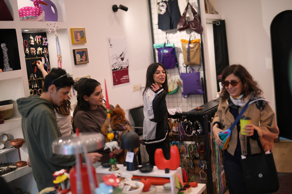 A shop owner, center, gestures as customers look around a gift shop in central Tehran, Iran, Wednesday, April 8, 2026. (AP Photo/Francisco Seco)