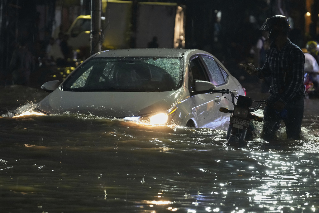 People in car drive and a motorcyclist pushes is vehicle through a flooded road caused by heavy rain in Lahore, Pakistan, Monday, Sept. 8, 2025. (AP Photo/K.M. Chaudary)