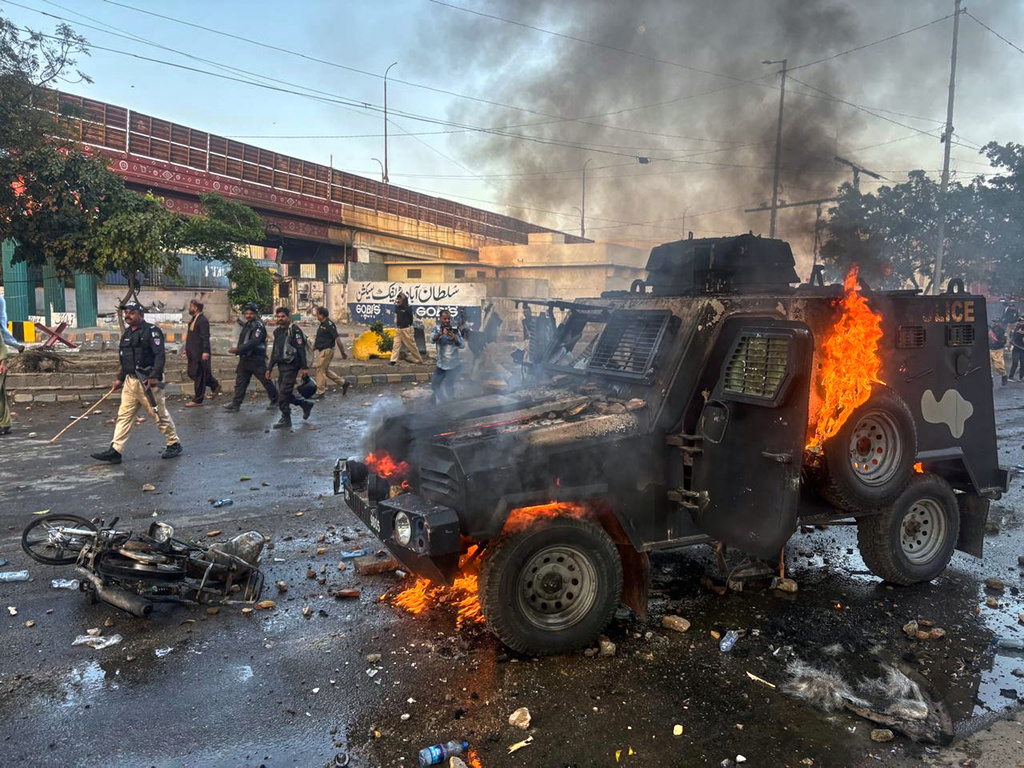 Paramilitary soldiers and police officers walk past a burning police's armoured vehicle, which was set on fire by Shiite Muslims during a protest over the killing of Iranian Supreme Leader Ayatollah Ali Khamenei, in Karachi, Pakistan, Sunday, March 1, 2026. (AP Photo/Muhammad Farooq)